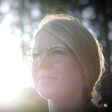 Blonde Frau mit Brille lächelt in Richtung der Sonne, Hintergrund unscharf.