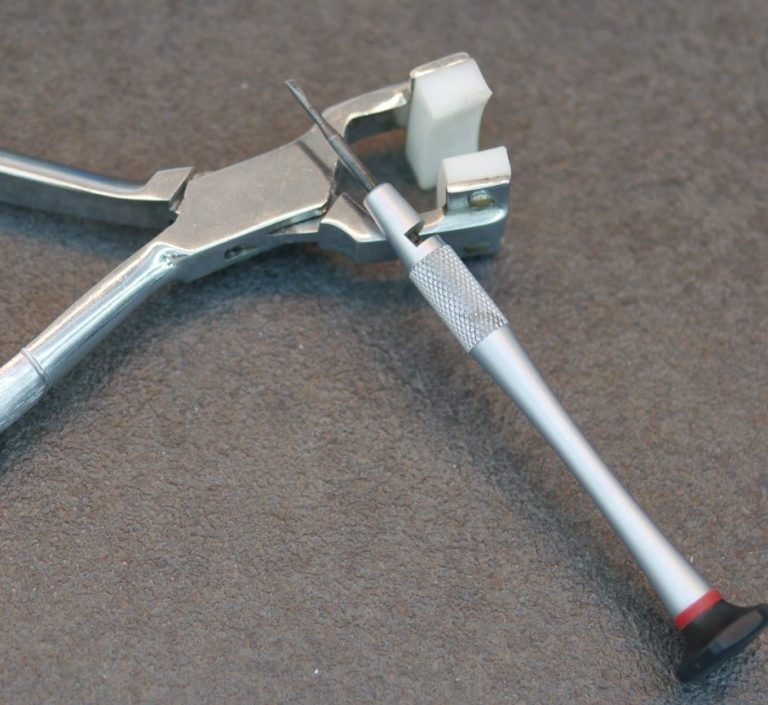 Zange mit einem weißen und roten Stift, auf grauem Untergrund.